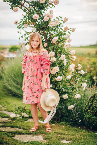 Summer portrait of pretty little girl wearing red stripe dress, posing in rose garden - Fotografie, Obrázek