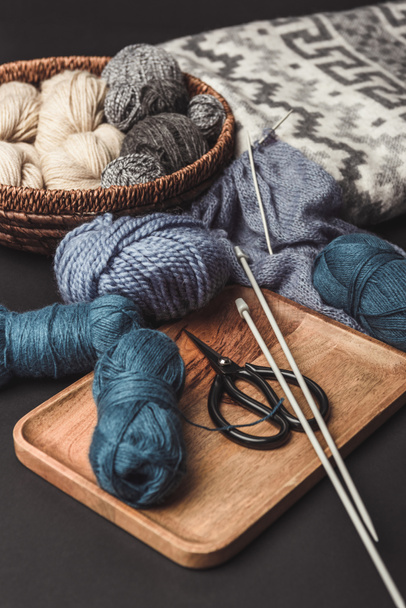 vista de perto de tricô, tesoura e agulhas de tricô em mesa escura com cobertor
 - Foto, Imagem