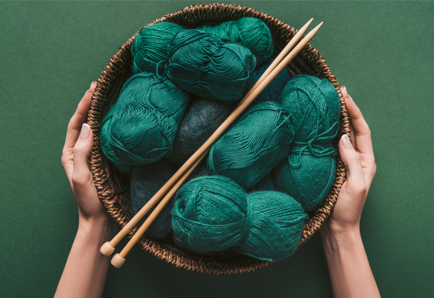 plan recadré de femme tenant panier en osier avec fil et aiguilles à tricoter sur fond vert
 - Photo, image