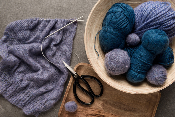 couché plat avec des boules de fil violet et bleu avec des ciseaux et des aiguilles à tricoter sur fond gris
 - Photo, image
