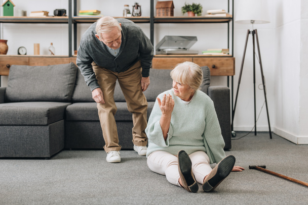 retired husband coming to upset senior wife sitting on floor with walking cane  - Φωτογραφία, εικόνα