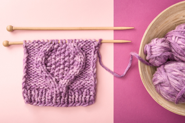flat lay with purple yarn clews in bowl and knitting needles on pink and purple backdrop - Fotó, kép