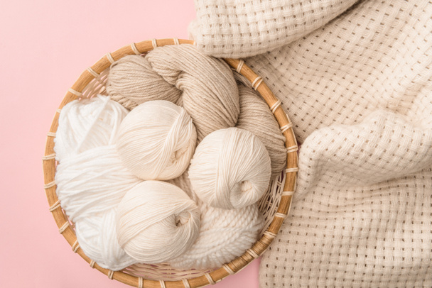 top view of yarn in wicker basket on pink background with knitted blanket  - Photo, Image
