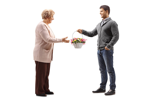 Full length shot of a young man giving abasket of flowers to an elderly woman isolated on white background - Valokuva, kuva