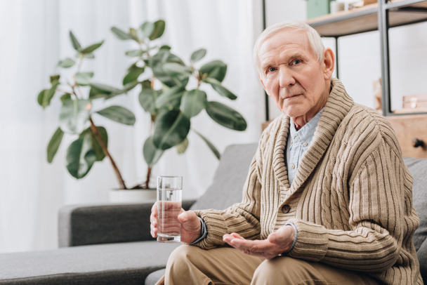 hombre mayor sosteniendo píldoras y vaso de agua y mirando a la cámara
 - Foto, imagen