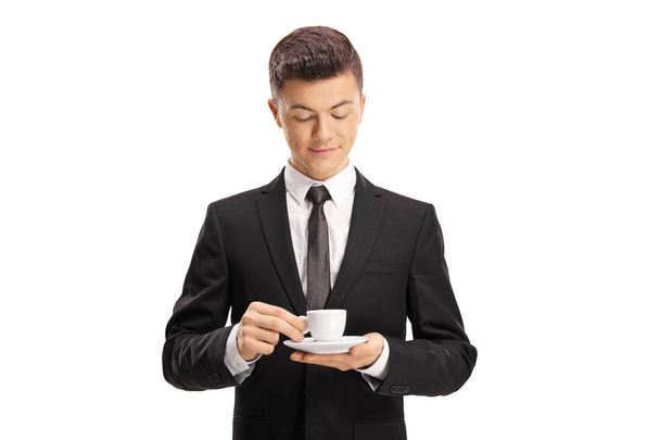 Young man in a suit holding an espresso coffee cup and looking at it isolated on white background - Φωτογραφία, εικόνα