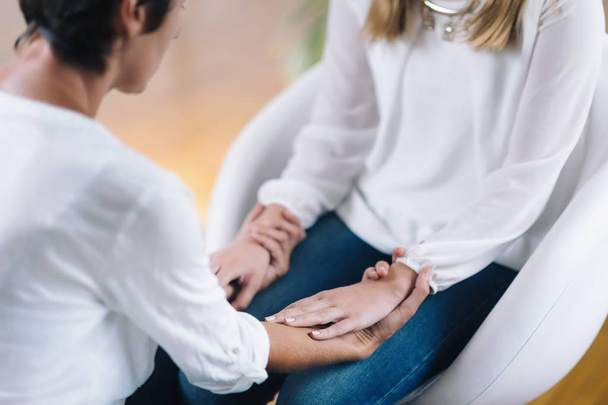 Female Theta healing therapist performing alternative therapy treatment with young woman patient. Therapist holding hands and transfer energy. Wearing white clothes. - Photo, Image