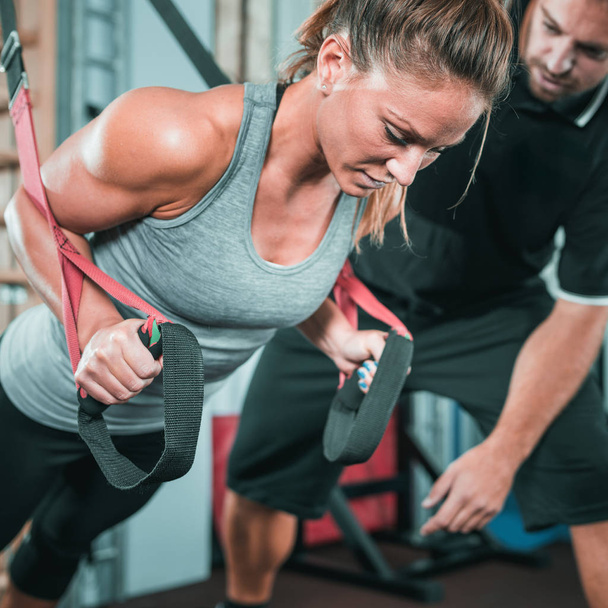 Personal trainer exercising on TRX with woman in the gym - Photo, Image