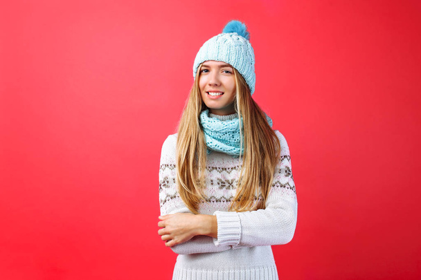 Beautiful girl standing isolated on red background, in warm blue hat and warm scarf. Concept, winter, cold, warm clothes - Fotografie, Obrázek