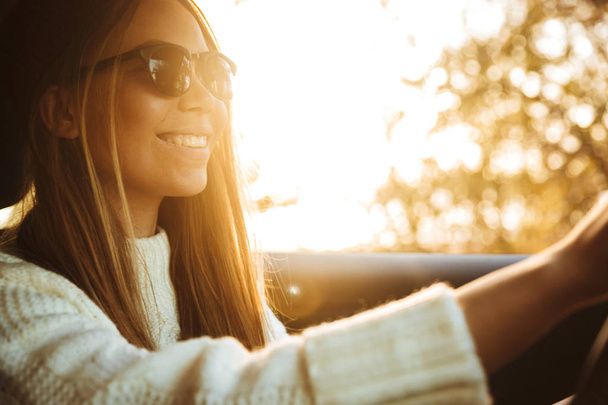 Smiling young girl driving a car during sunset - Fotó, kép