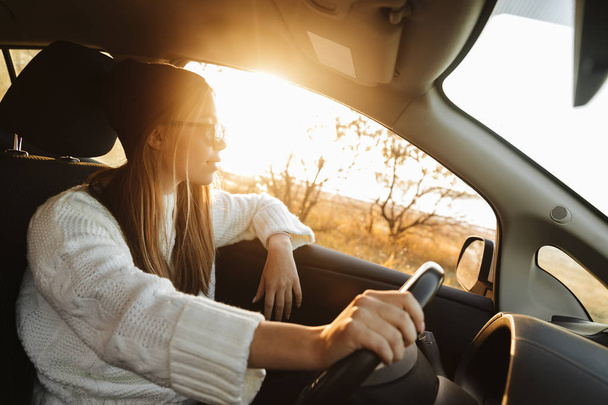 Smiling young girl driving a car during sunset - Foto, imagen