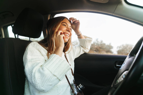 Krásná mladá žena mluví na mobilním telefonu, zatímco sedí v autě - Fotografie, Obrázek