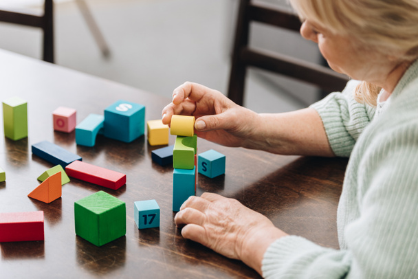 senior woman playing with wooden cubes on table - Photo, Image