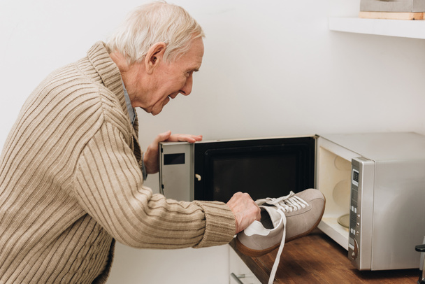 retired man with dementia disease putting shoe in microwave oven  - Foto, afbeelding