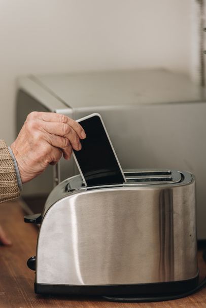 cropped view of senior man putting smartphone in toaster  - Photo, Image