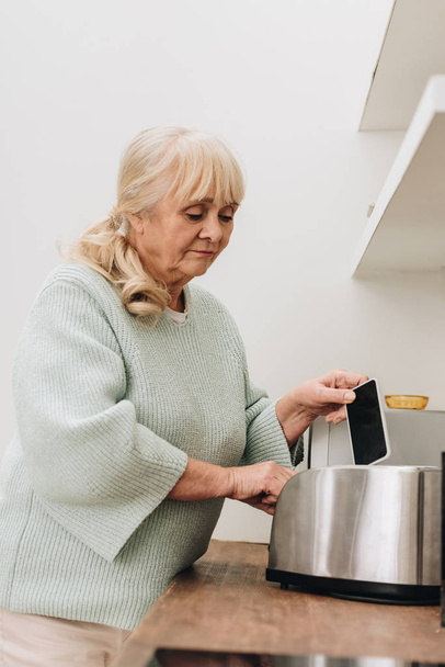retired woman with dementia disease putting smartphone in toaster  - Photo, Image