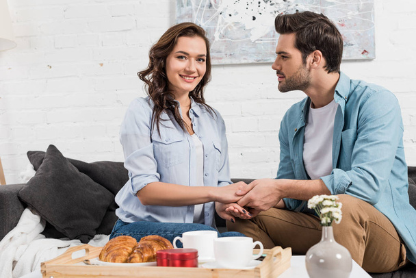 couple sitting on couch and holding hands while having breakfast at home  - Φωτογραφία, εικόνα