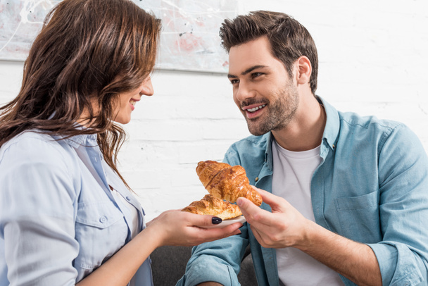 beautiful couple looking at each other and eating croissants during breakfast at home  - Photo, Image