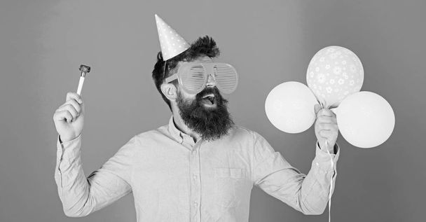 Man with beard and mustache on happy face holds air balloons, blue background. Guy in party hat with holiday attributes celebrates. Hipster in giant eyeglasses celebrating birthday. Party concept - Valokuva, kuva