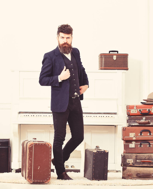 Man, traveller with beard and mustache with luggage, luxury white interior background. Macho elegant on strict face standing near pile of vintage suitcase. Luggage and travelling concept - Foto, immagini