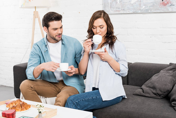 couple sitting on couch and drinking coffee during breakfast at home - Fotoğraf, Görsel