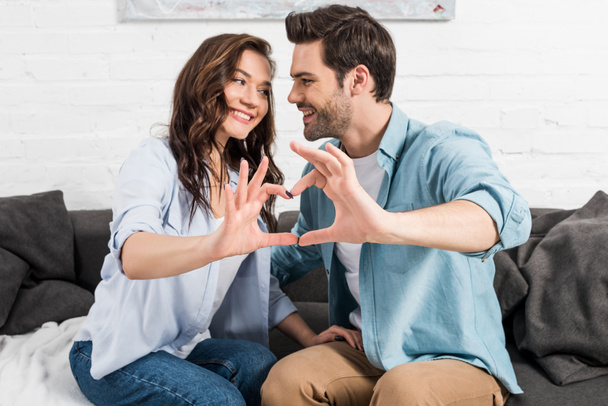 ευτυχισμένο ζευγάρι σε casual ρούχα δείχνουν σύμβολο καρδιά με τα χέρια στο σπίτι  - Φωτογραφία, εικόνα