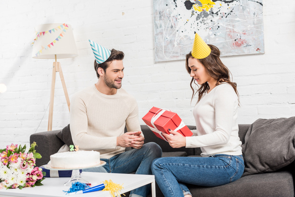couple celebrating birthday and man presenting birthday gift box to woman in living room - Foto, Imagem