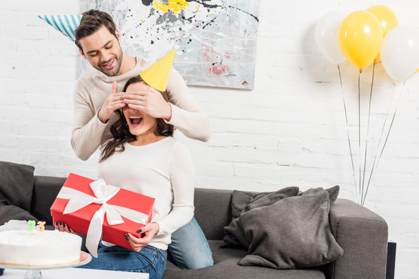 man surprising excited woman with birthday gift in living room - Zdjęcie, obraz