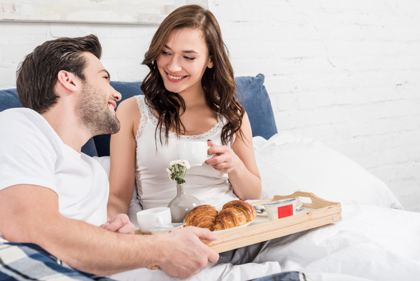 smiling couple lying in bed and having breakfast in morning - Fotó, kép