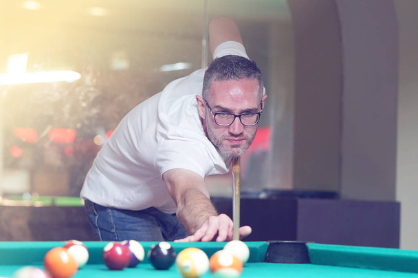 Male plays a billiard at the club. Caucasian mcaucasianan playing spending time on recreation. Play and fun concept. Toning - Photo, Image