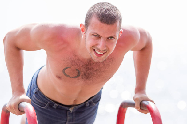 Handsome young man doing street workout on the beach in a bright summer day.  - Photo, Image