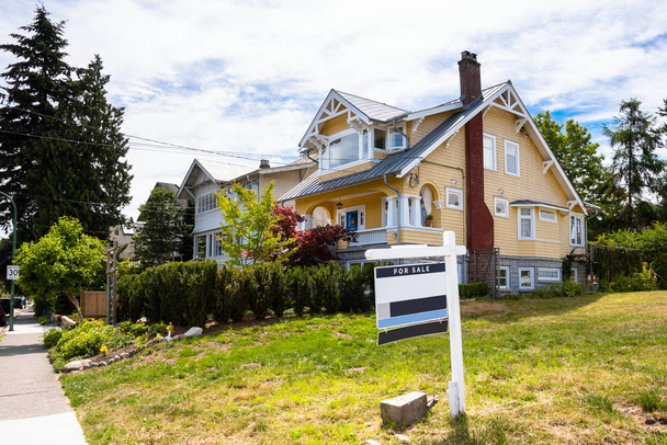 Знак продажи недвижимости во дворе вдоль улицы с традиционными американскими домами на заднем плане
 - Фото, изображение