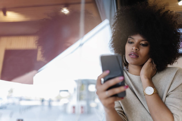 Portrait of attractive afro woman using mobile phone at the coffee shop. Business woman concept - Fotó, kép
