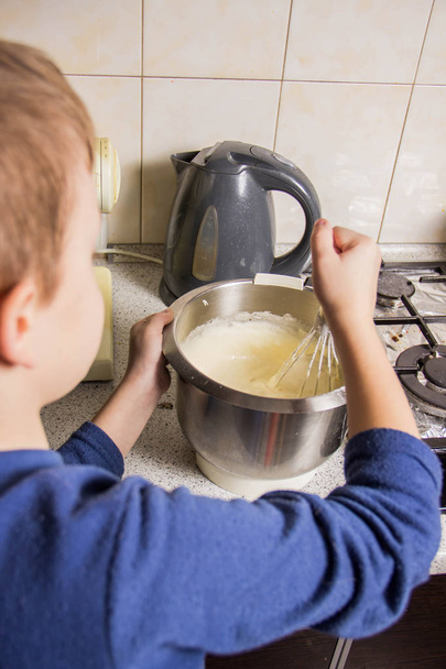 A boy in the kitchen kneading a dough for chocolate cupcakes - Foto, imagen