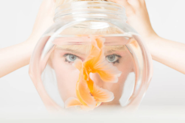 Portrait of a beautiful girl with a goldfish in an aquarium. - Foto, afbeelding