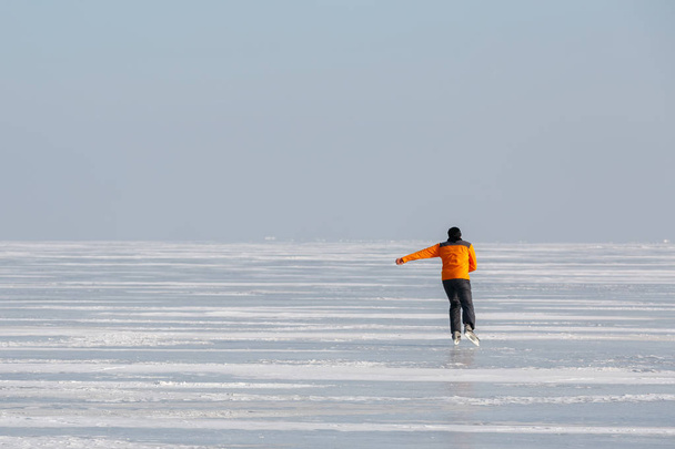 junger Mann in orangefarbenem Sweatshirt läuft allein auf dem Eis einer zugefrorenen Meeresbucht - Foto, Bild