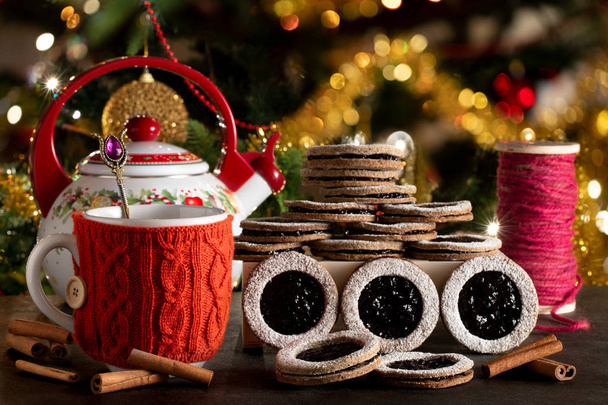 Galletas caseras con mermelada de arándanos servidas con té en ambiente navideño con árbol decorado en el fondo
. - Foto, Imagen