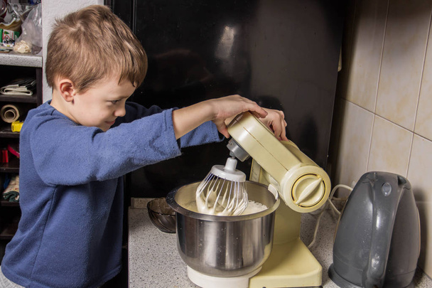 Un garçon dans la cuisine pétrissant une pâte pour des cupcakes au chocolat
 - Photo, image