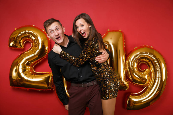 Pari kaveri tyttö kiiltävä glitter mekko, musta paita juhlii loma puolue eristetty kirkkaan punainen seinä tausta kultainen numerot ilmapalloja studio muotokuva. Hyvää uutta vuotta 2019 Joulukonsepti
 - Valokuva, kuva