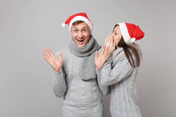 Feliz diversión pareja chica chico en rojo Santa Navidad sombrero suéteres grises bufandas aisladas en fondo de pared gris, retrato de estudio. Feliz Año Nuevo 2019 celebración fiesta concepto. Simular espacio de copia
 - Foto, imagen