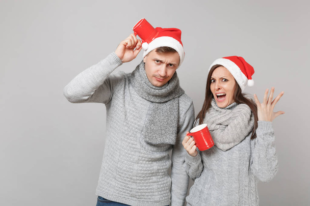 Весело пара дівчина хлопець в червоний Різдво Санта hat сірі светри шарфи утримуйте чашки чаю ізольовані на фоні сірих стін, студія портрет. Щасливого нового року 2019 свято партії концепція. Макету копію простір - Фото, зображення