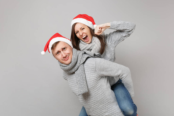fröhliche lustige paar Mädchen Kerl in roten Weihnachtsmann Mütze graue Pullover Schals isoliert auf grauem Wandhintergrund, Studio-Porträt. Frohes neues Jahr 2019 Feier Feiertag Party-Konzept. Attrappe Kopierraum - Foto, Bild