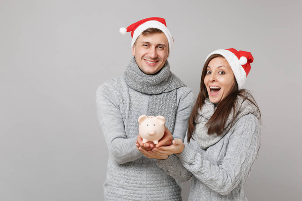 Paar Mädchen Kerl in roter Weihnachtsmütze graue Pullover Schals halten Schweinchen isoliert auf grauen Wandhintergrund Studio-Porträt. Frohes neues Jahr 2019 Feier Feiertag Party-Konzept. Attrappe Kopierraum - Foto, Bild