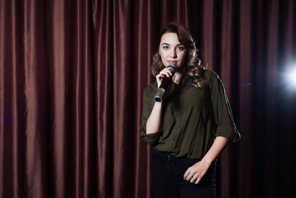 A woman singing on stage in the microphone karaoke on the background of red curtains - 写真・画像