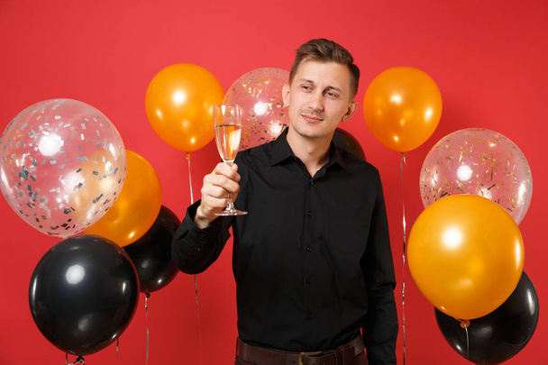 赤い背景の気球に手にシャンパンのグラスを黒のクラシック シャツの若い美男子。国際女性の日、幸せな新年、誕生日モックアップ休日党概念 - 写真・画像