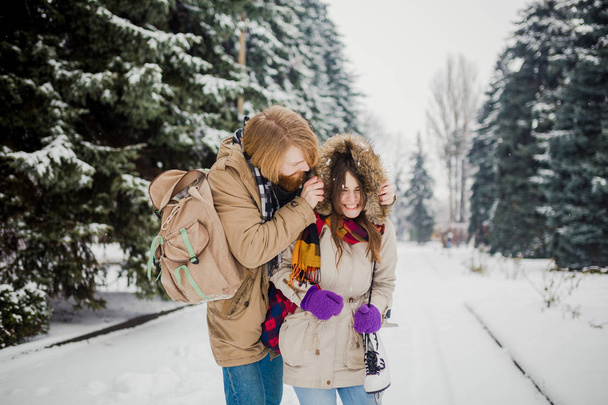 Mooie jonge Kaukasische mensen (echt) paar liefhebbers op een datum in winter park. Een man met een baard, schaatsen en een rugzak hugs, een man houdt een vrouw een datum Valentijnsdag in de natuur. - Foto, afbeelding