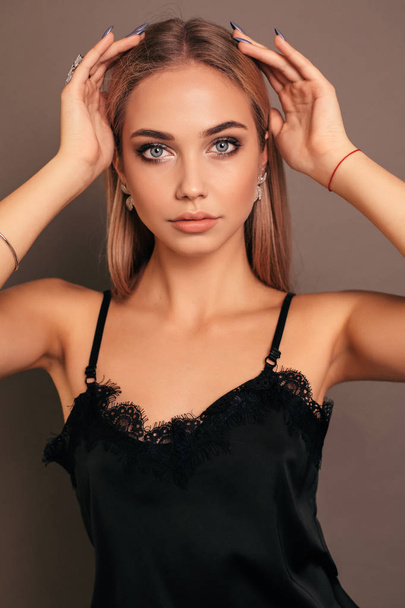 fashion photo of beautiful young girl with blond hair in elegant black dress with jewelry posing in studio - Photo, image
