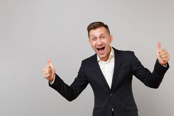 Portrait of happy young business man in classic black suit, shirt showing thumb up screaming isolated on grey wall background in studio. Achievement career wealth business concept. Mock up copy space - Φωτογραφία, εικόνα