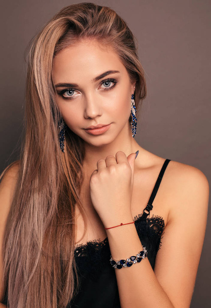 fashion photo of beautiful young girl with blond hair in elegant black dress with jewelry posing in studio - Zdjęcie, obraz