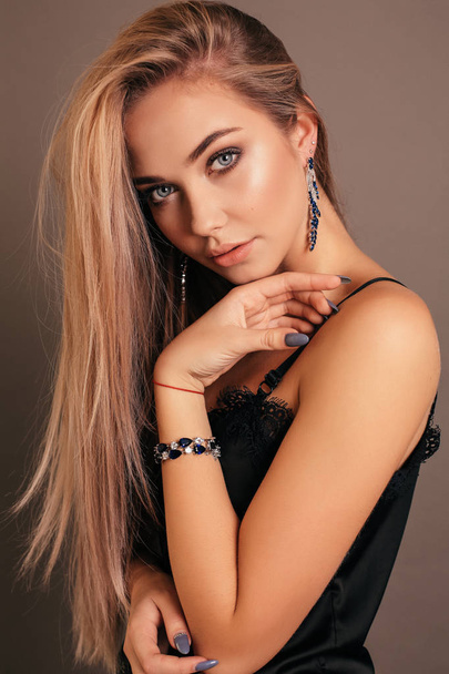 fashion photo of beautiful young girl with blond hair in elegant black dress with jewelry posing in studio - Zdjęcie, obraz